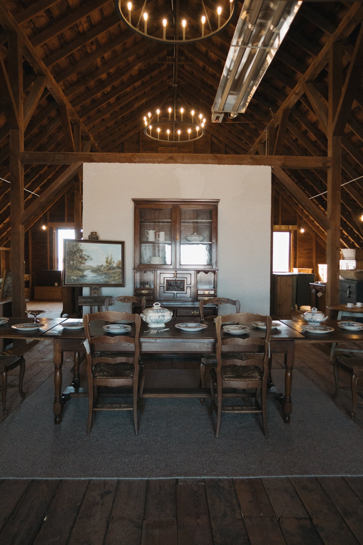 An antique pine hutch and farmhouse dining table set beneath candle chandeliers in the Marvella Mercantile barn