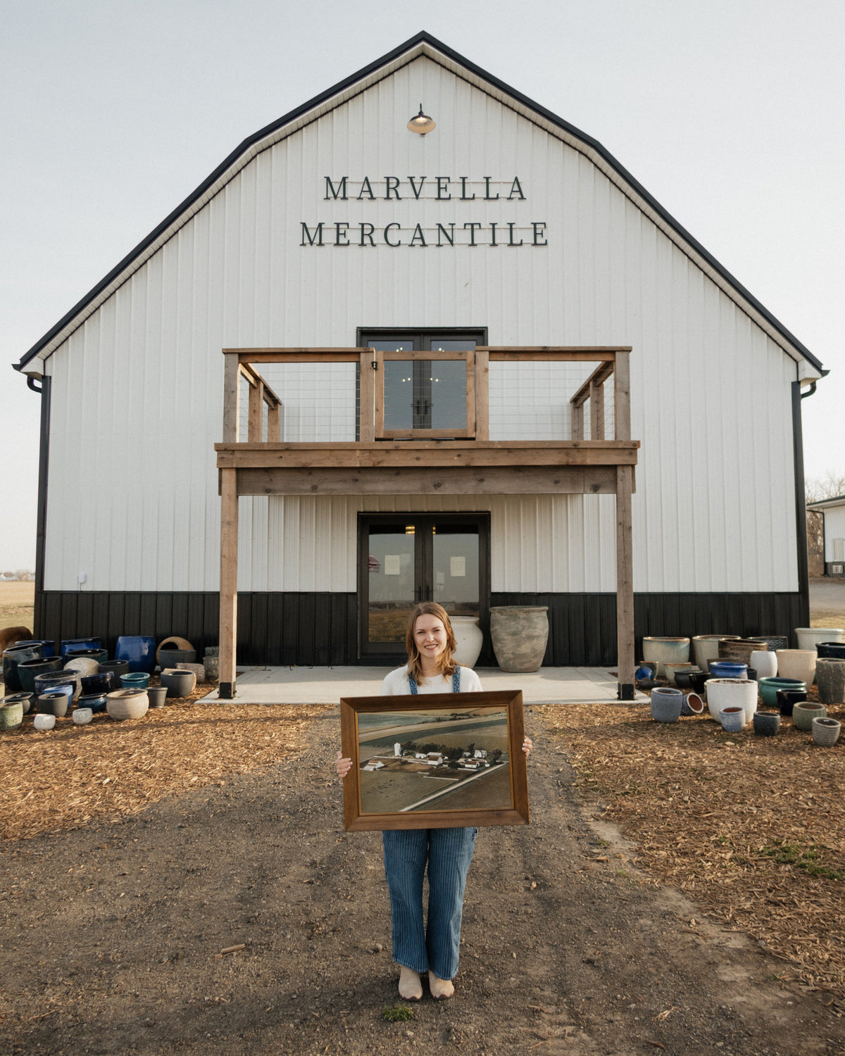 A woman holds a framed antique painting in front of the Marvella Mercantile barn in Yutan, Nebraska