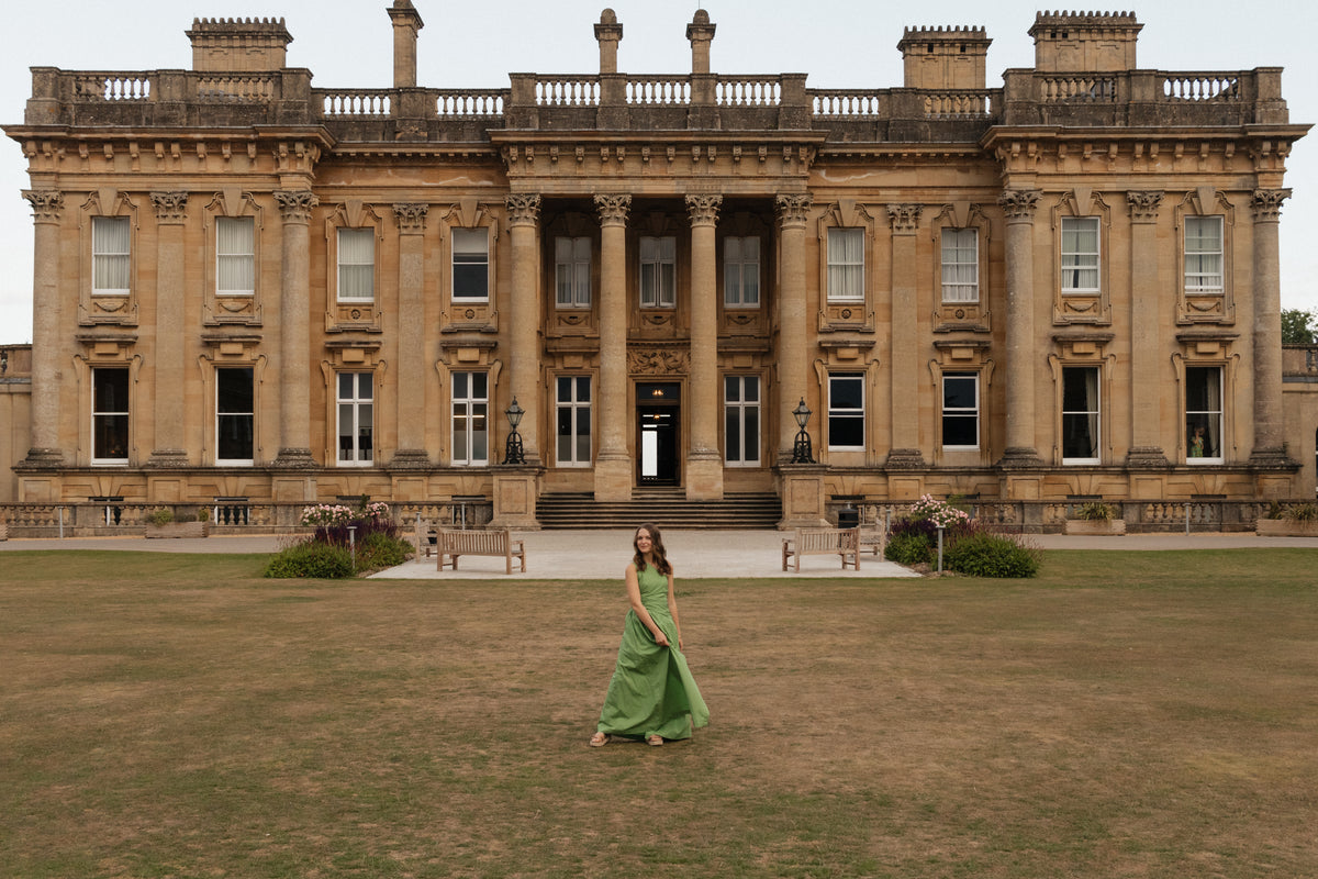 A woman in a green dress crosses the lawn of a grand English stately home on an antique sourcing trip