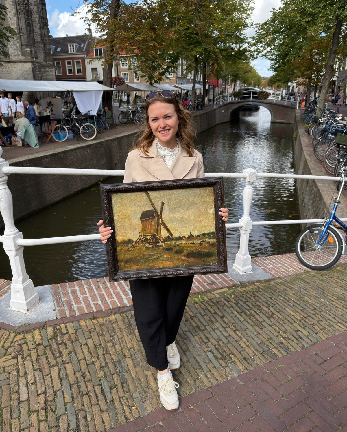 A woman holds a framed antique windmill painting beside a canal in the Netherlands