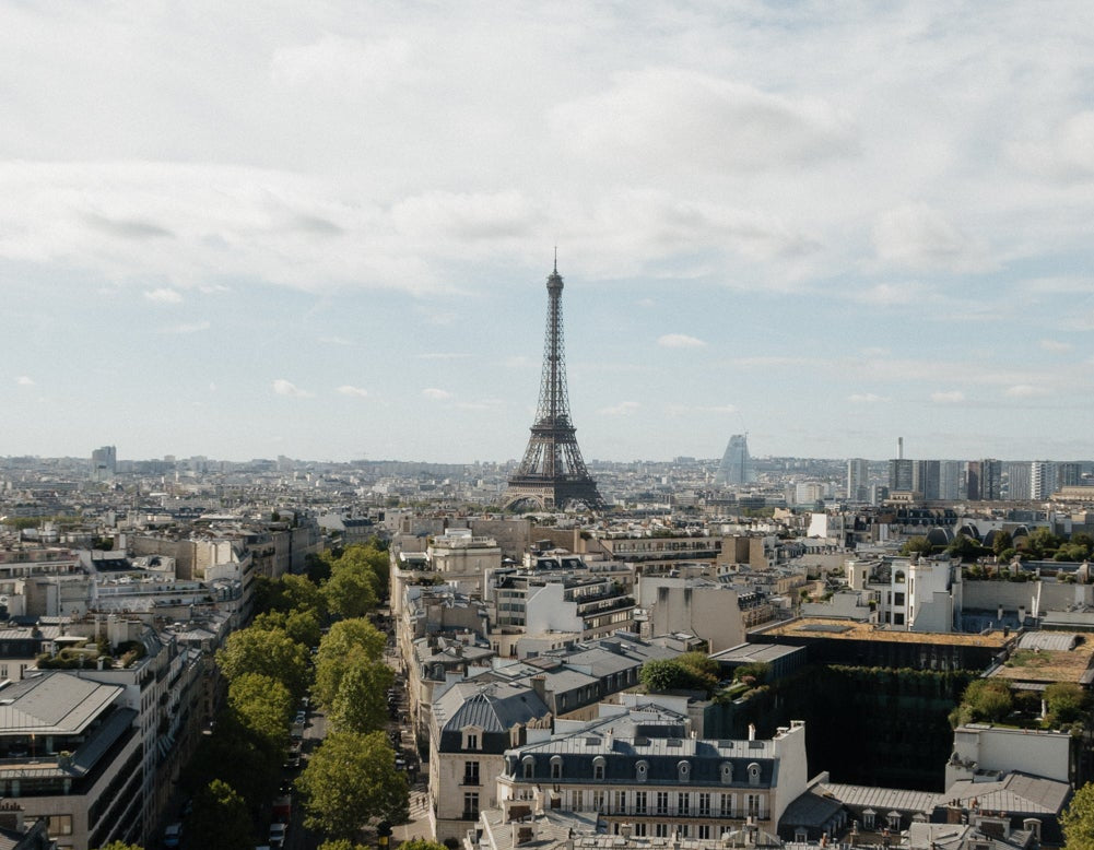 The Eiffel Tower rising above Paris rooftops and a tree-lined avenue
