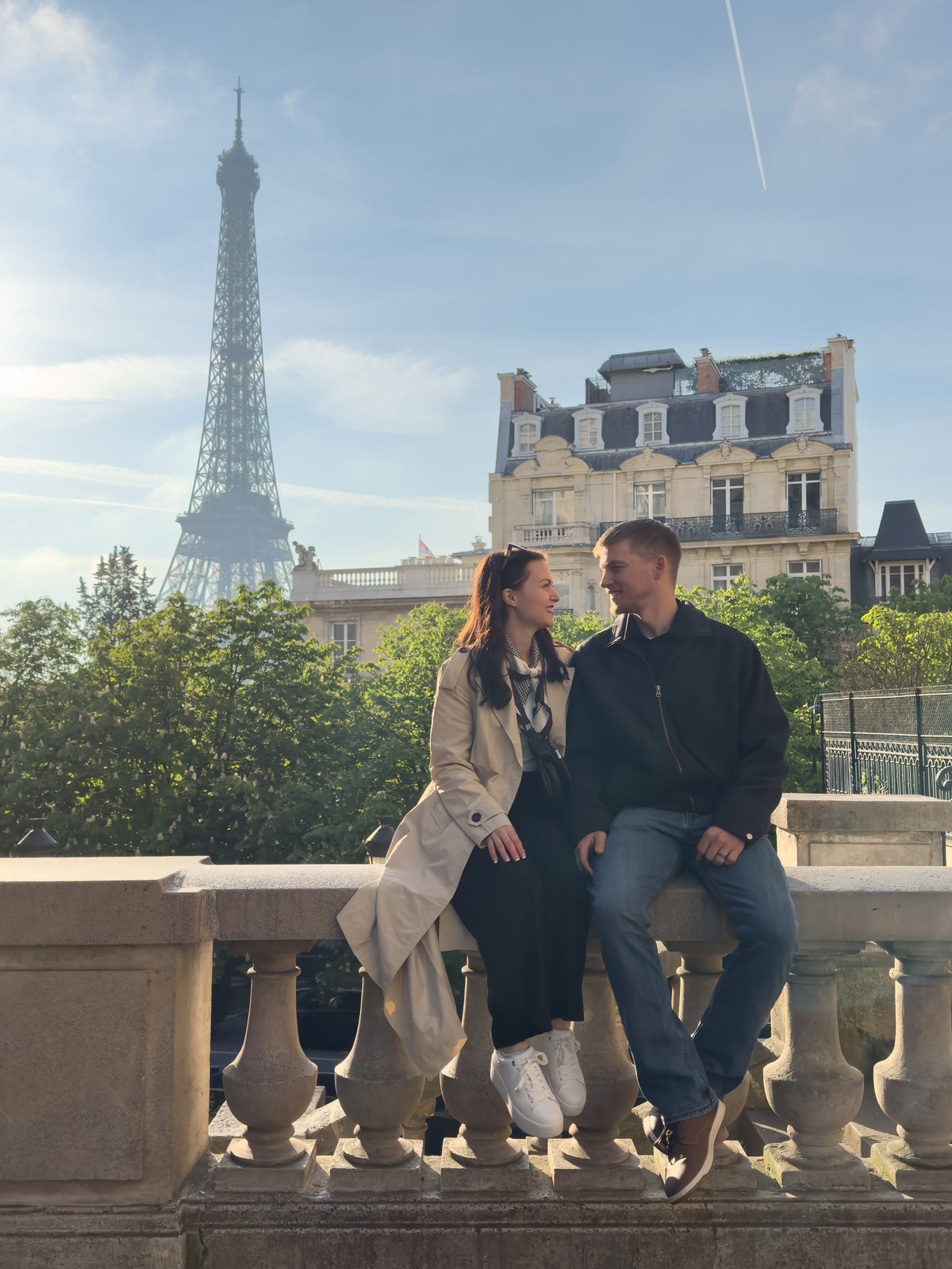 A couple sits on a stone balustrade in Paris with the Eiffel Tower behind them