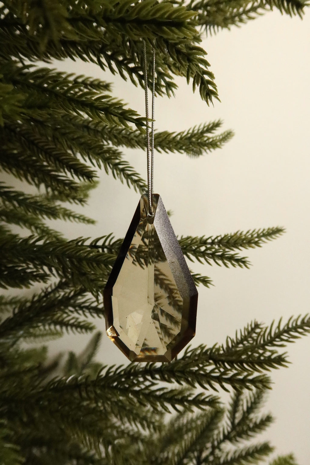 Faceted point amber glass drop ornament on a silver cord hanging on a Christmas tree