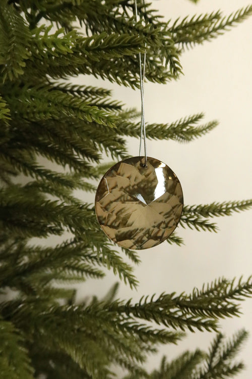 Round amber faceted glass Christmas ornament on a silver cord hanging on an evergreen tree