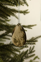 Teardrop shaped amber faceted glass ornament hanging among green pine branches