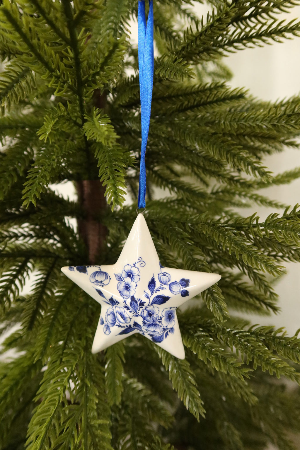 Delft blue floral star ornament on a blue ribbon among green pine branches