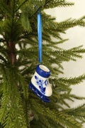 Delft blue and white ceramic ice skate Christmas ornament with a hand-painted floral design hanging from a blue ribbon on an evergreen tree