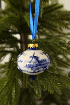 Front view of the Delft blue windmill drop ornament with gold cap and blue tip among green pine branches