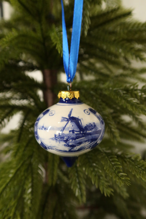 Front view of the Delft blue windmill drop ornament with gold cap and blue tip among green pine branches