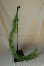 59 inch faux Norfolk pine garland hanging from a black stand and draping onto the floor
