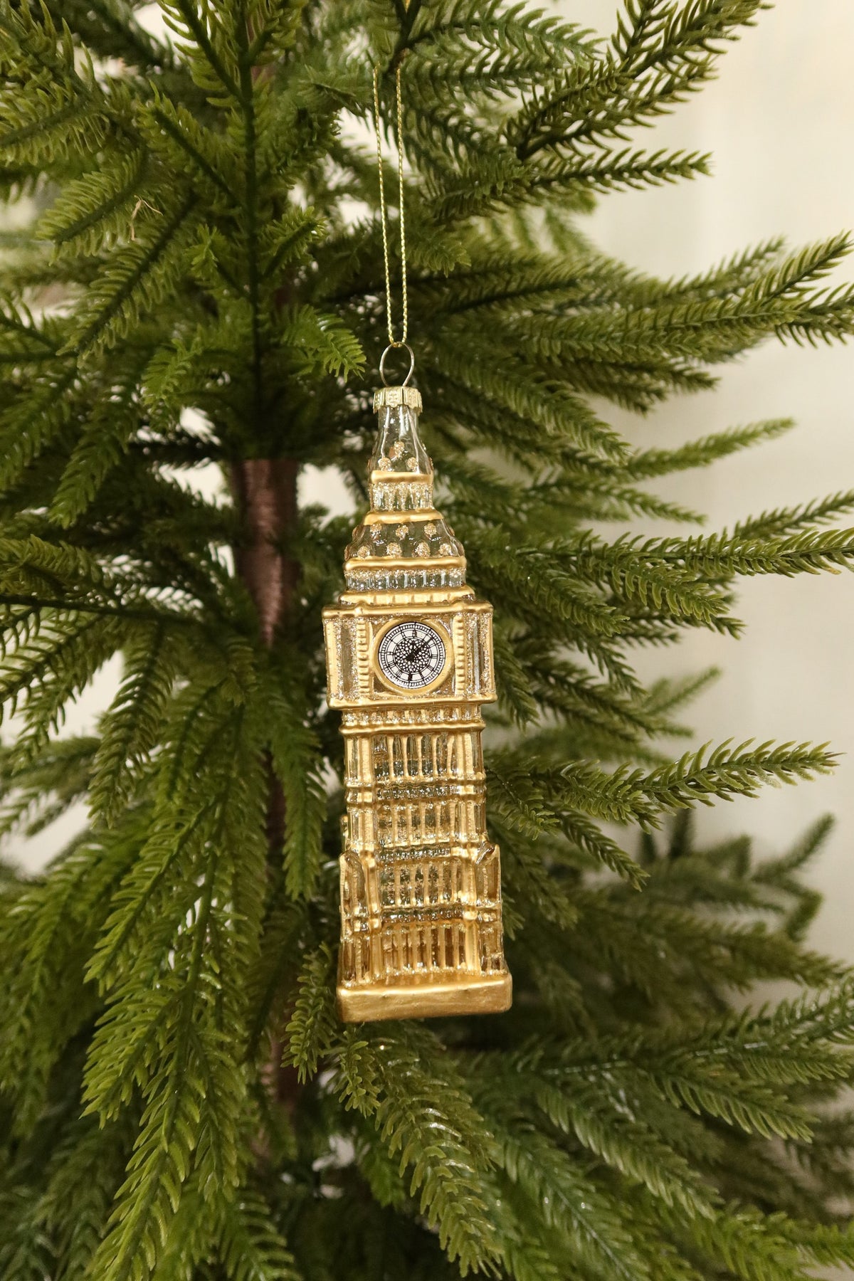 Glass Big Ben clock tower Christmas ornament in clear and gold with glitter detail hanging on an evergreen tree