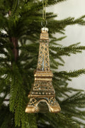 Clear glass Eiffel Tower Christmas ornament with gold lattice and glitter detail hanging on an evergreen tree