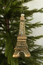 Clear glass Eiffel Tower Christmas ornament with gold lattice and glitter detail hanging on an evergreen tree