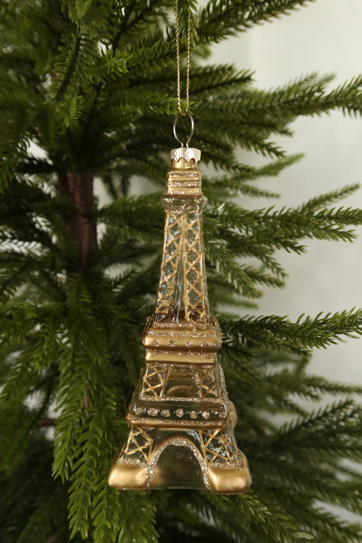 Glass Eiffel Tower ornament on a gold cord among green pine branches