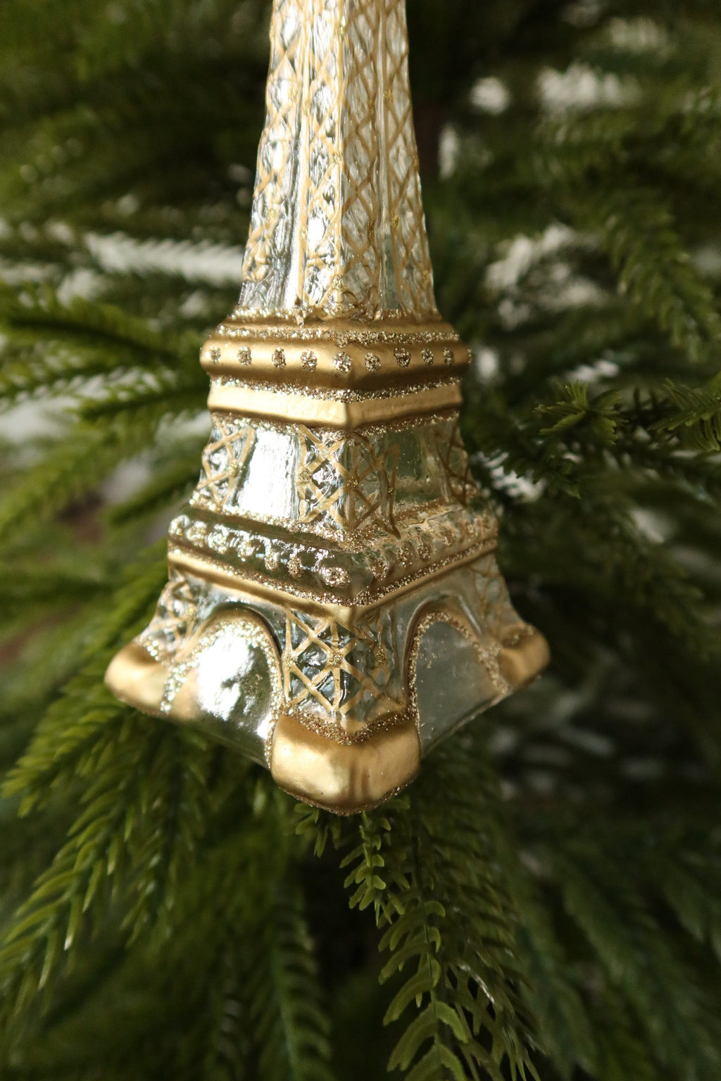 Angled view of the arched base and gold feet of the glass Eiffel Tower ornament