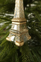 Angled view of the arched base and gold feet of the glass Eiffel Tower ornament