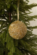 Gold glass bead ball Christmas ornament with a beaded branch design hanging from a gold ribbon on an evergreen tree