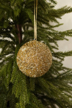 Gold glass bead ball Christmas ornament with a beaded branch design hanging from a gold ribbon on an evergreen tree