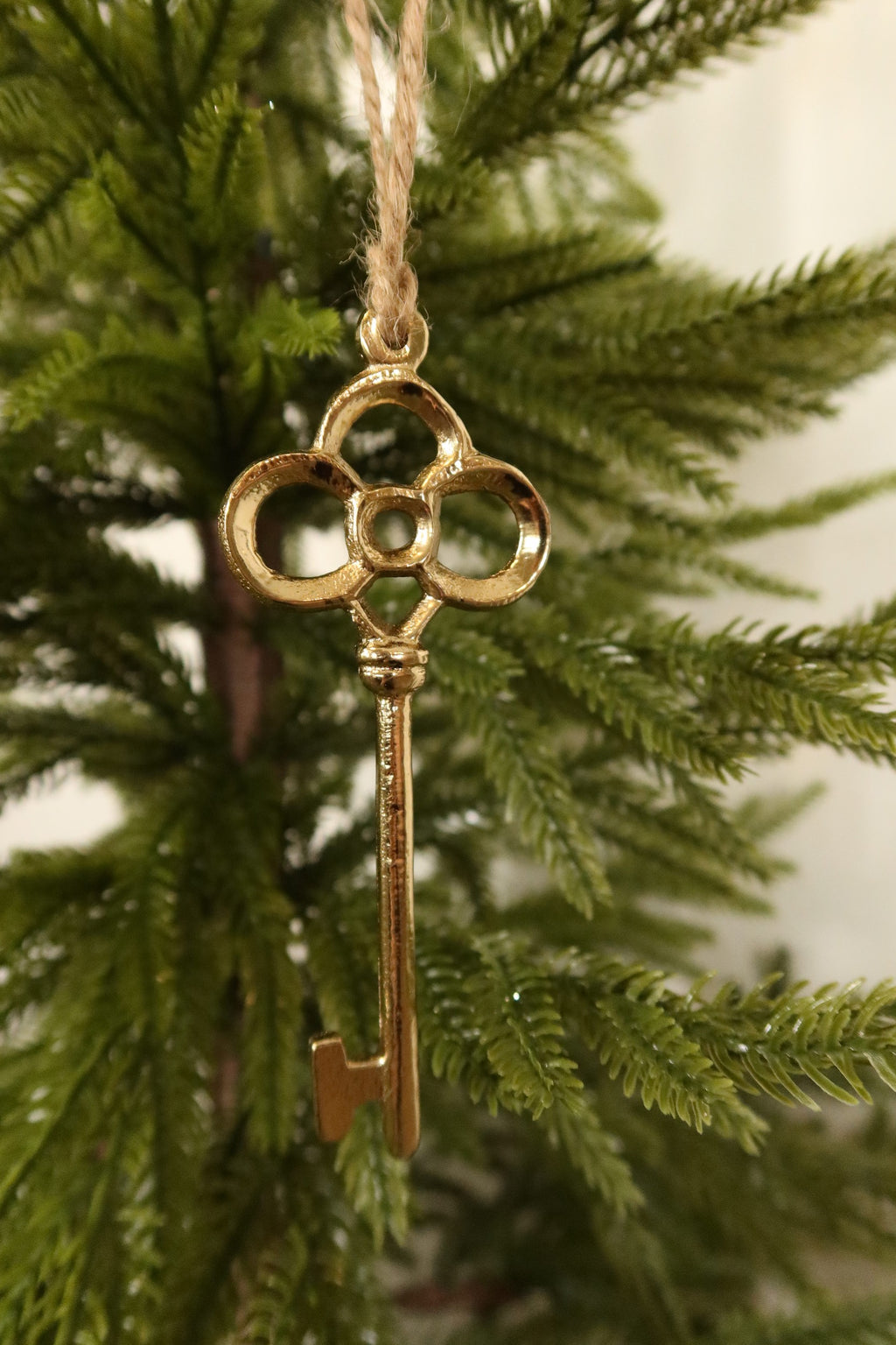 Gold key ornament with clover bow on jute twine among green pine branches