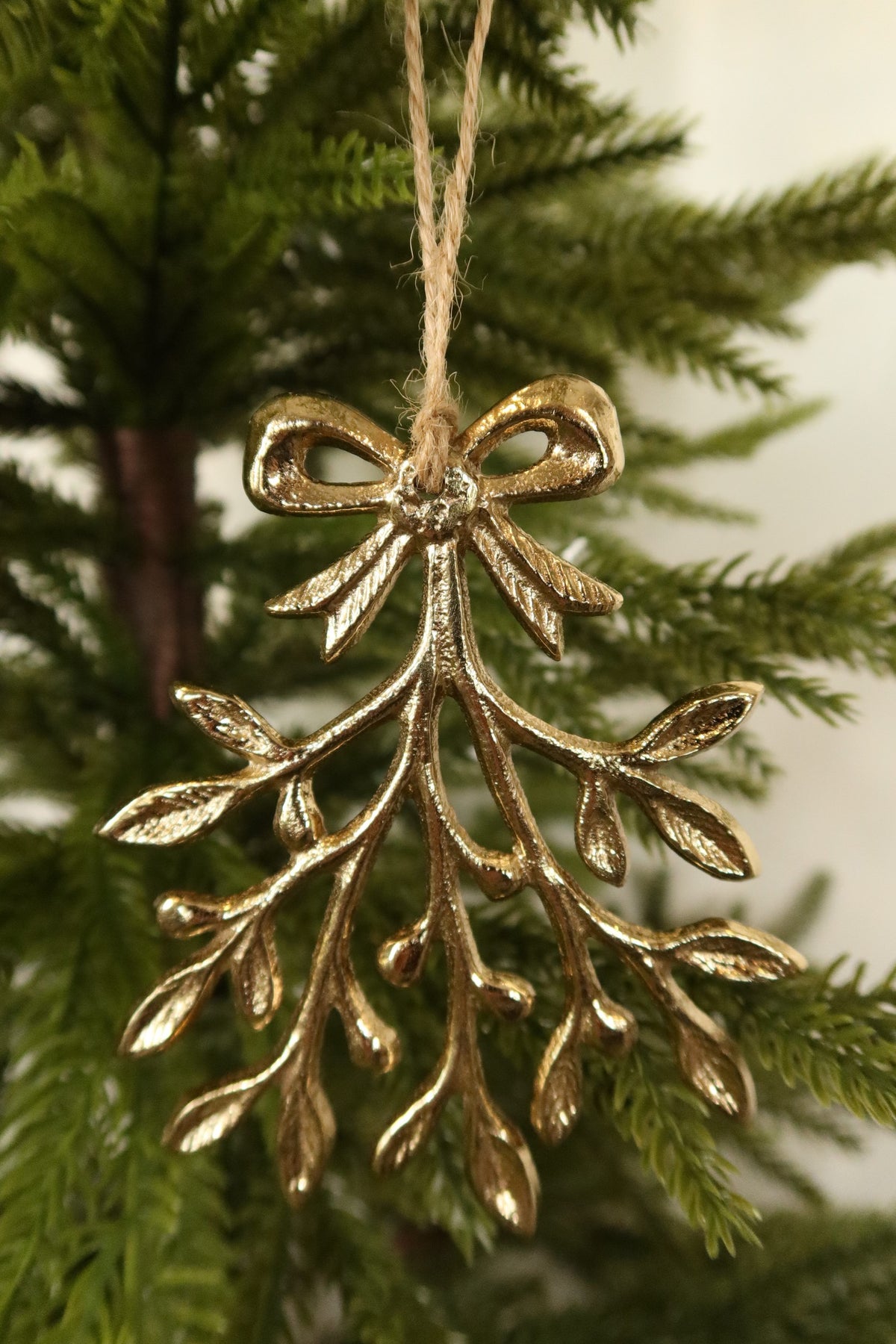 Closer view of the gold mistletoe ornament showing its leafy branches and berry details against green pine