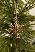 Polished gold metal snowflake Christmas ornament with branch-like arms hanging by jute twine on an evergreen tree