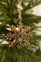Closer view of the 3 inch gold metal snowflake ornament on jute twine among green pine branches