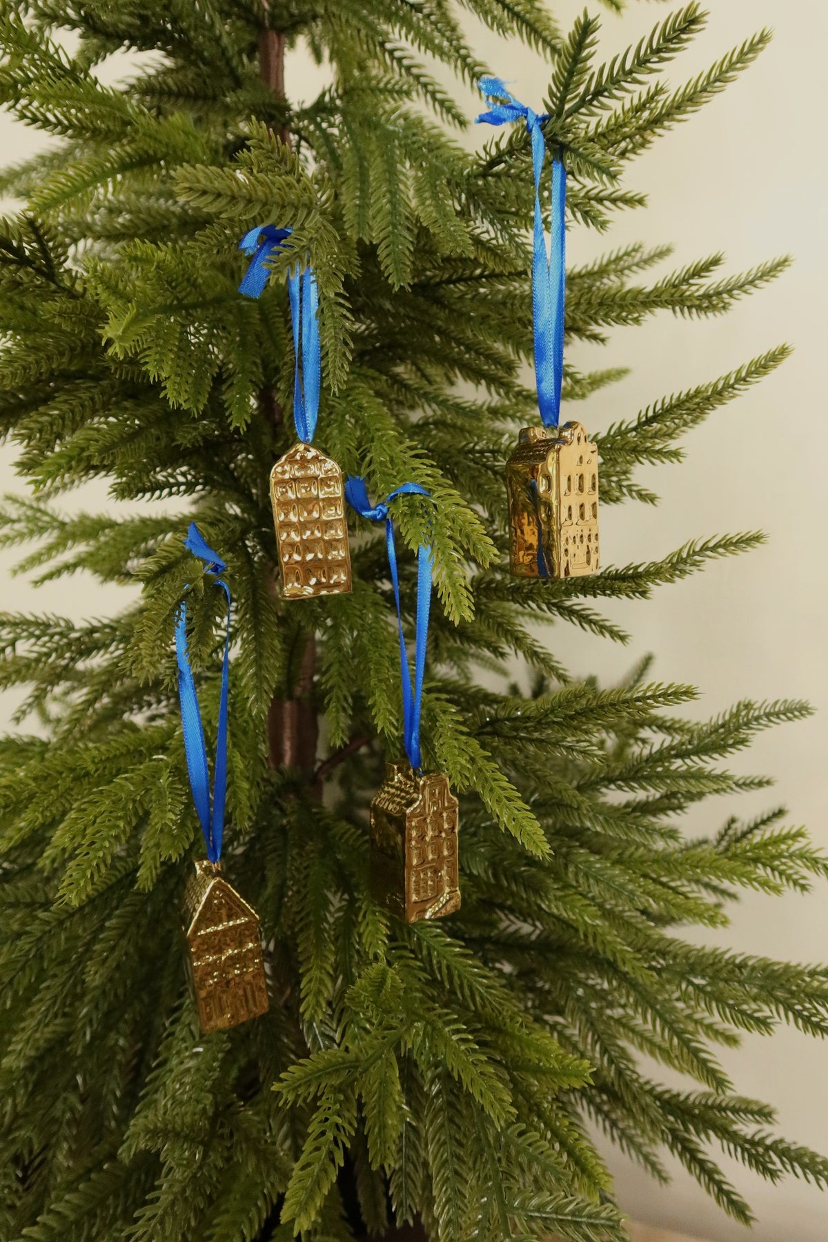 Four gold mini canal house ornaments in rounded, square, bell and pointed gable styles hanging together on a Christmas tree