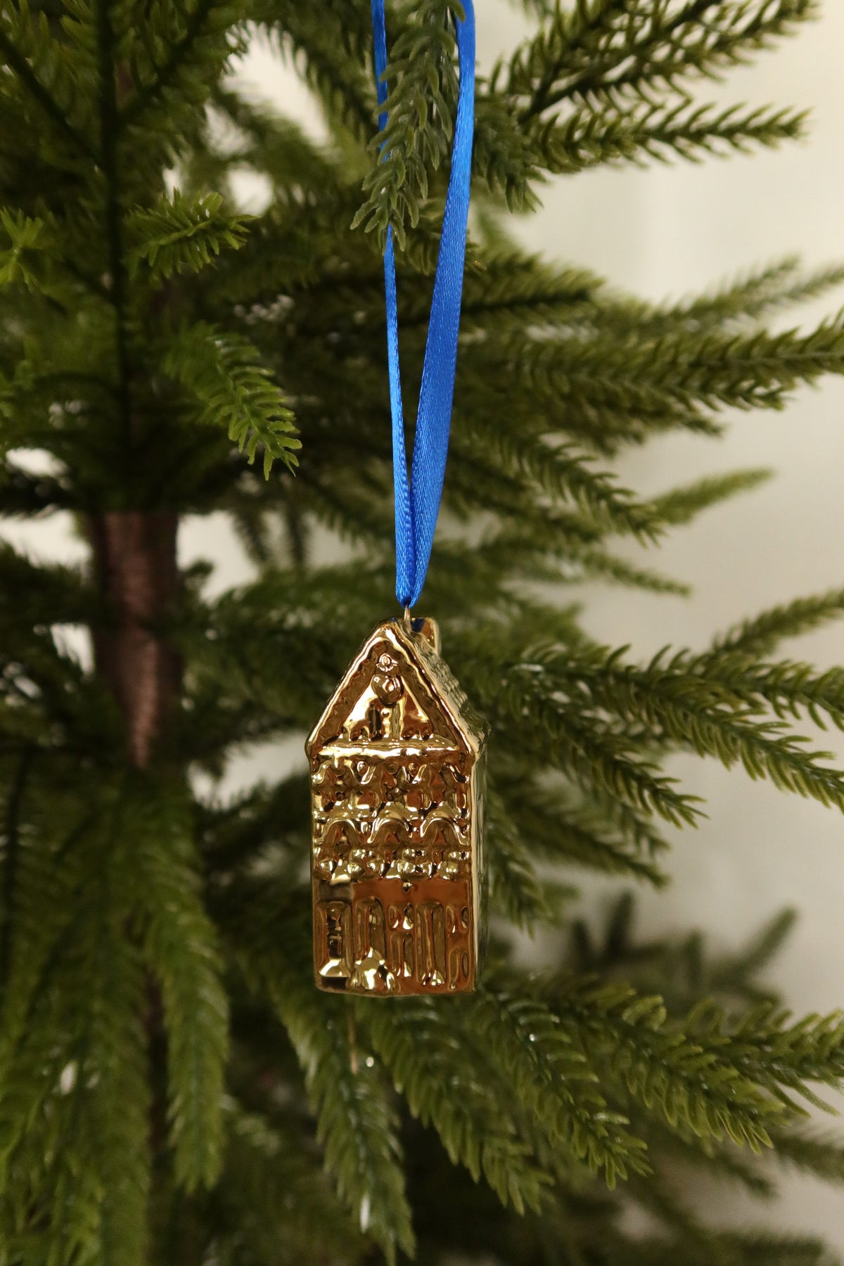 Gold mini canal house ornament with a pointed gable hanging from a blue ribbon on an evergreen tree