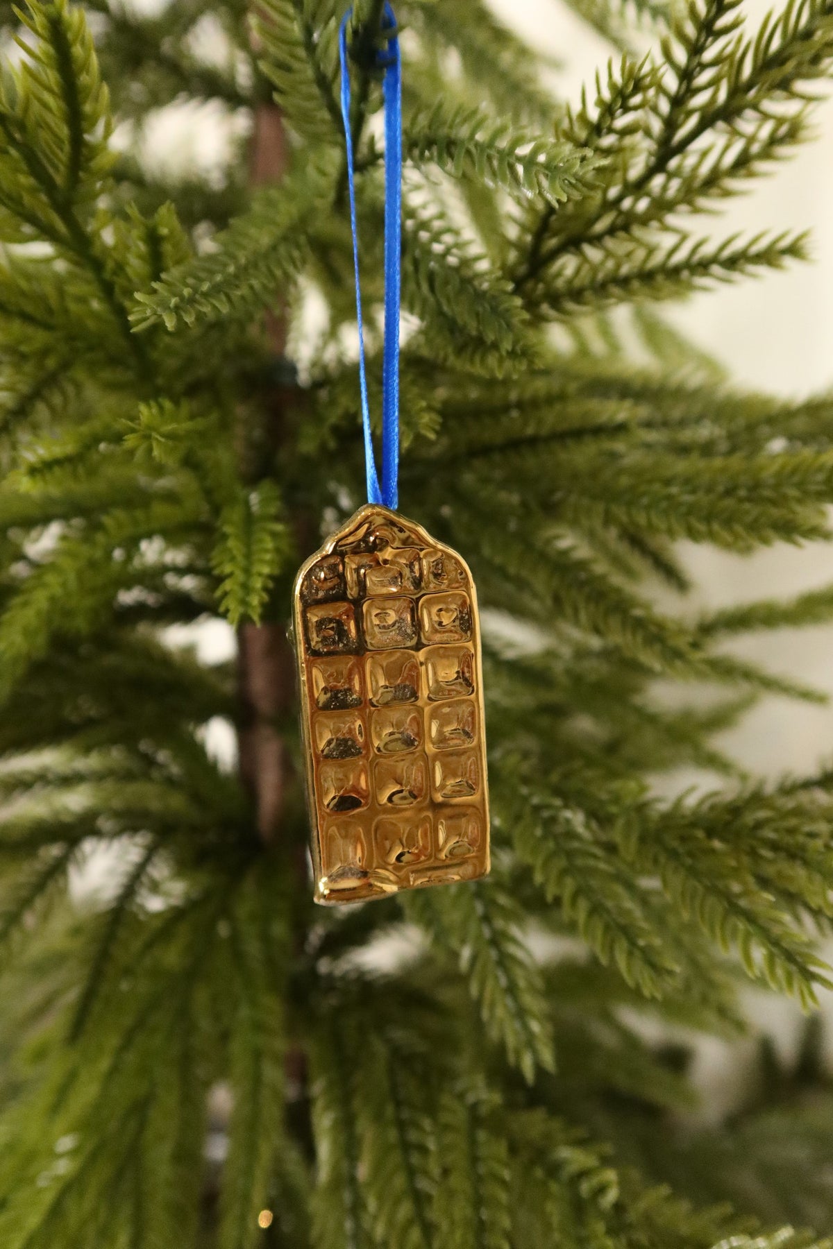 Gold mini Dutch canal house Christmas ornament with a rounded gable hanging from a blue ribbon on an evergreen tree