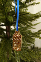 Gold mini canal house ornament with a square gable hanging from a blue ribbon on an evergreen tree