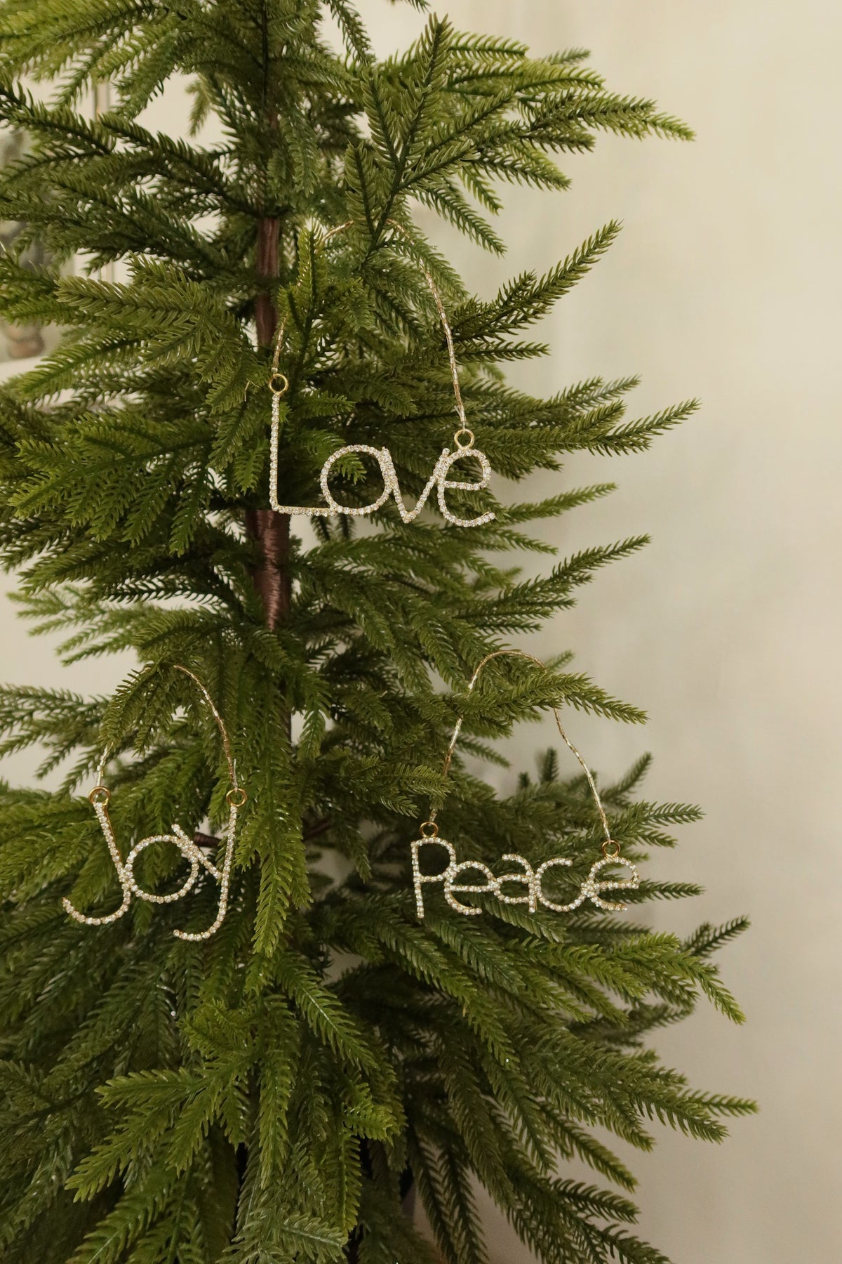 Gold rhinestone Joy, Love and Peace ornaments hanging together on a Christmas tree