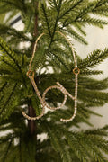 Gold rhinestone Joy script Christmas ornament hanging from a gold beaded strand on an evergreen tree