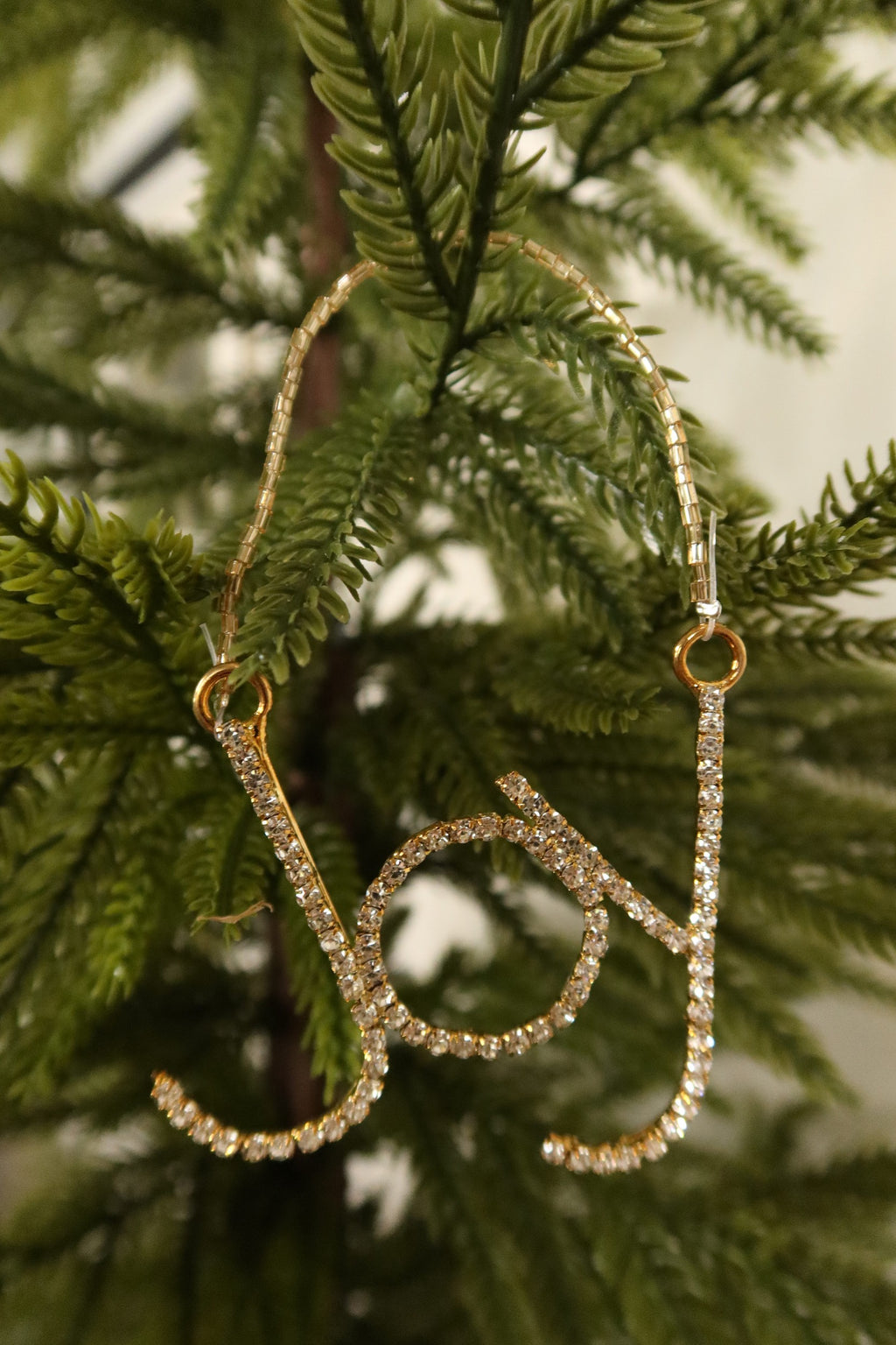 Closer view of the sparkling clear rhinestone Joy ornament in a gold setting against green pine