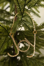 Closer view of the sparkling clear rhinestone Joy ornament in a gold setting against green pine