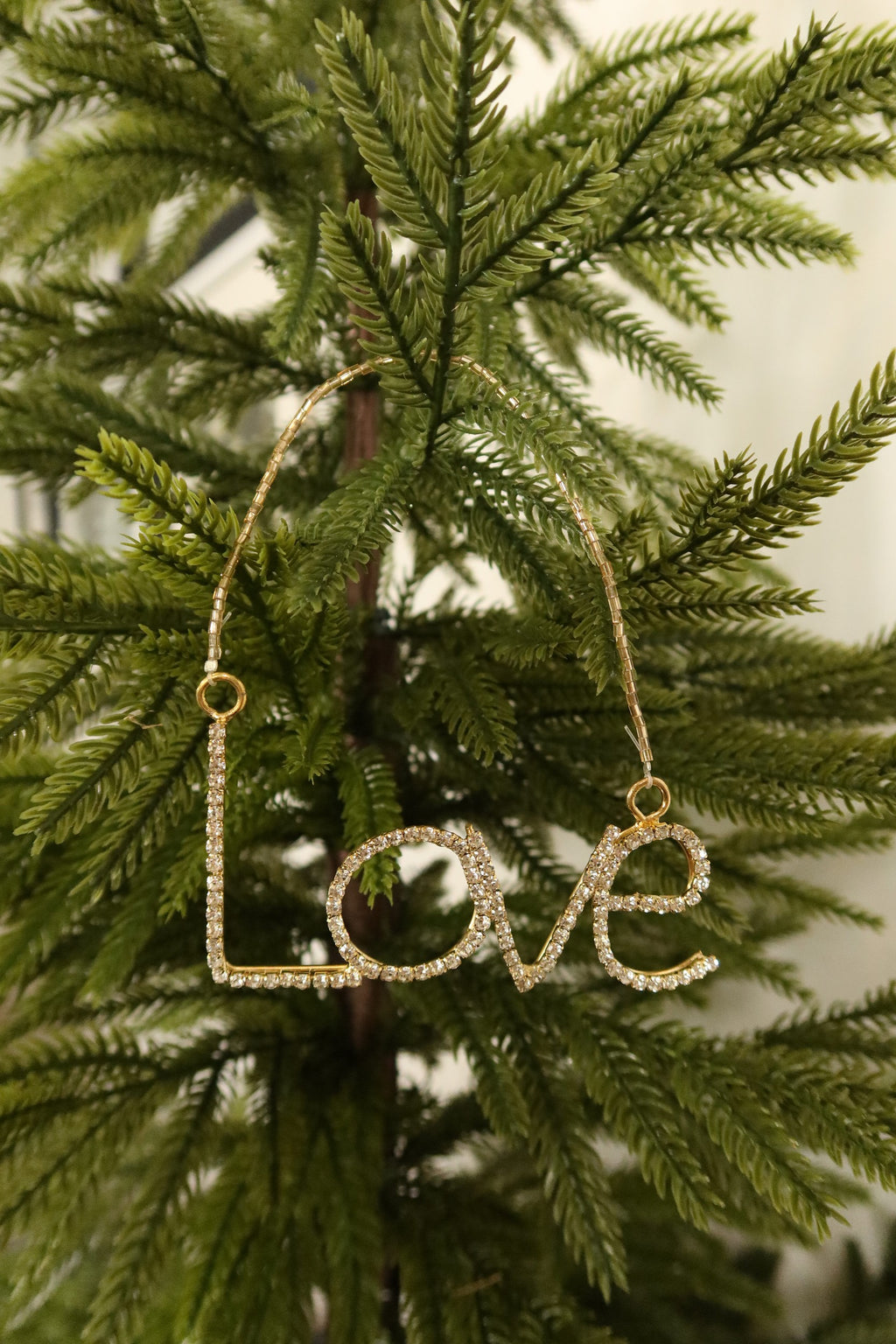 Gold rhinestone Love word Christmas ornament hanging from a gold beaded strand on an evergreen tree