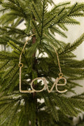 Gold rhinestone Love word Christmas ornament hanging from a gold beaded strand on an evergreen tree