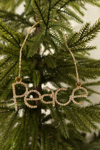 Gold rhinestone Peace word Christmas ornament hanging from a gold beaded strand on an evergreen tree