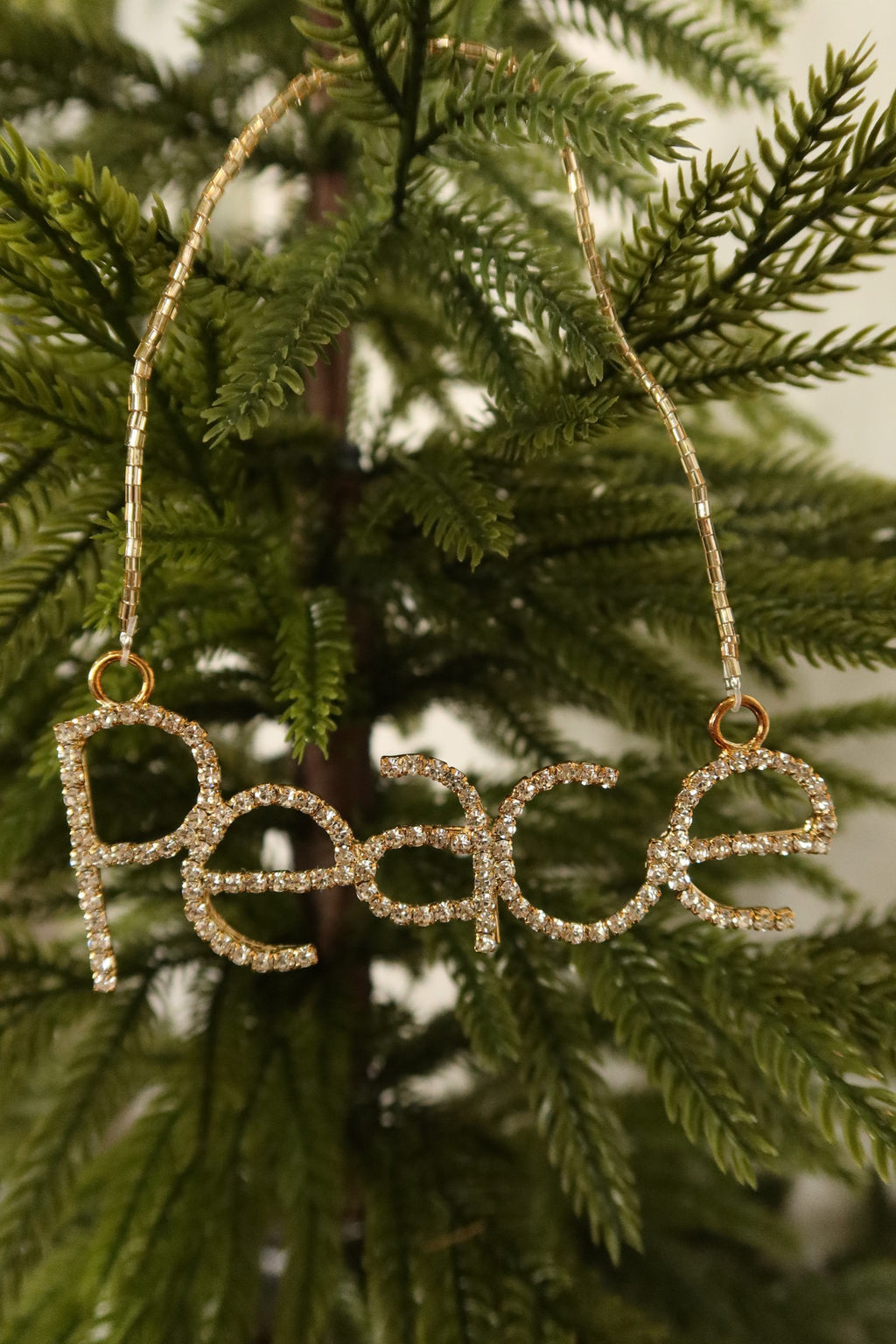 Closer view of the clear rhinestone Peace ornament in a gold setting against green pine