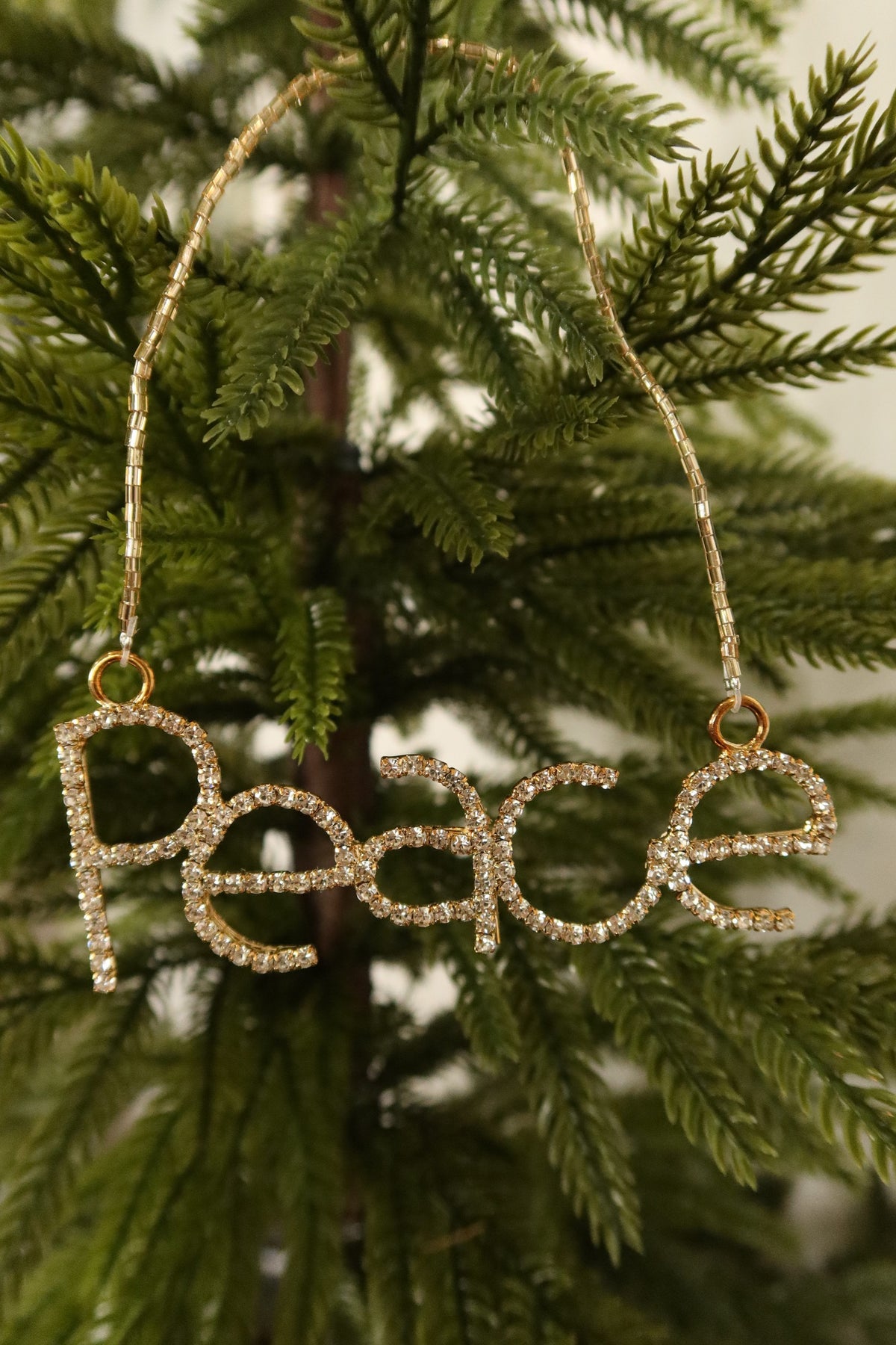 Closer view of the clear rhinestone Peace ornament in a gold setting against green pine