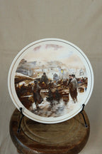 Vintage Hammersley bone china plate with a painterly winter Christmas market scene and fine gold rim, displayed on a black plate stand