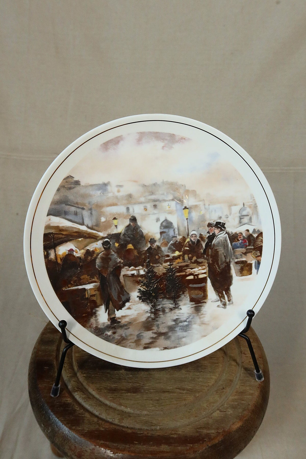 Vintage Hammersley bone china plate with a painterly winter Christmas market scene and fine gold rim, displayed on a black plate stand