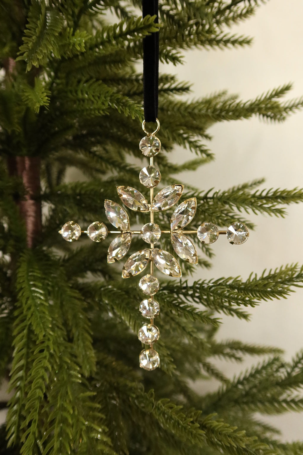 Jeweled cross Christmas ornament with clear marquise and round rhinestones in a gold setting hanging from a black velvet ribbon on an evergreen tree