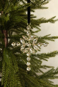 Jeweled cross Christmas ornament with clear marquise and round rhinestones in a gold setting hanging from a black velvet ribbon on an evergreen tree