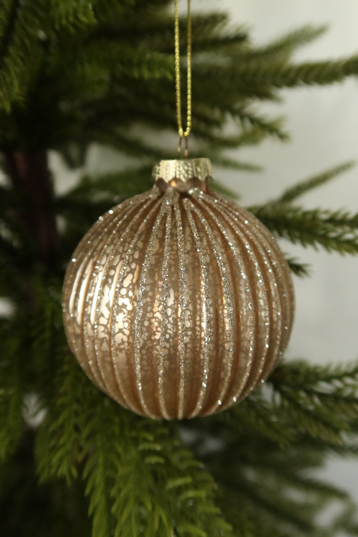 Closer view of the round matte gold fluted glass ball ornament showing its glitter ribs and gold cap