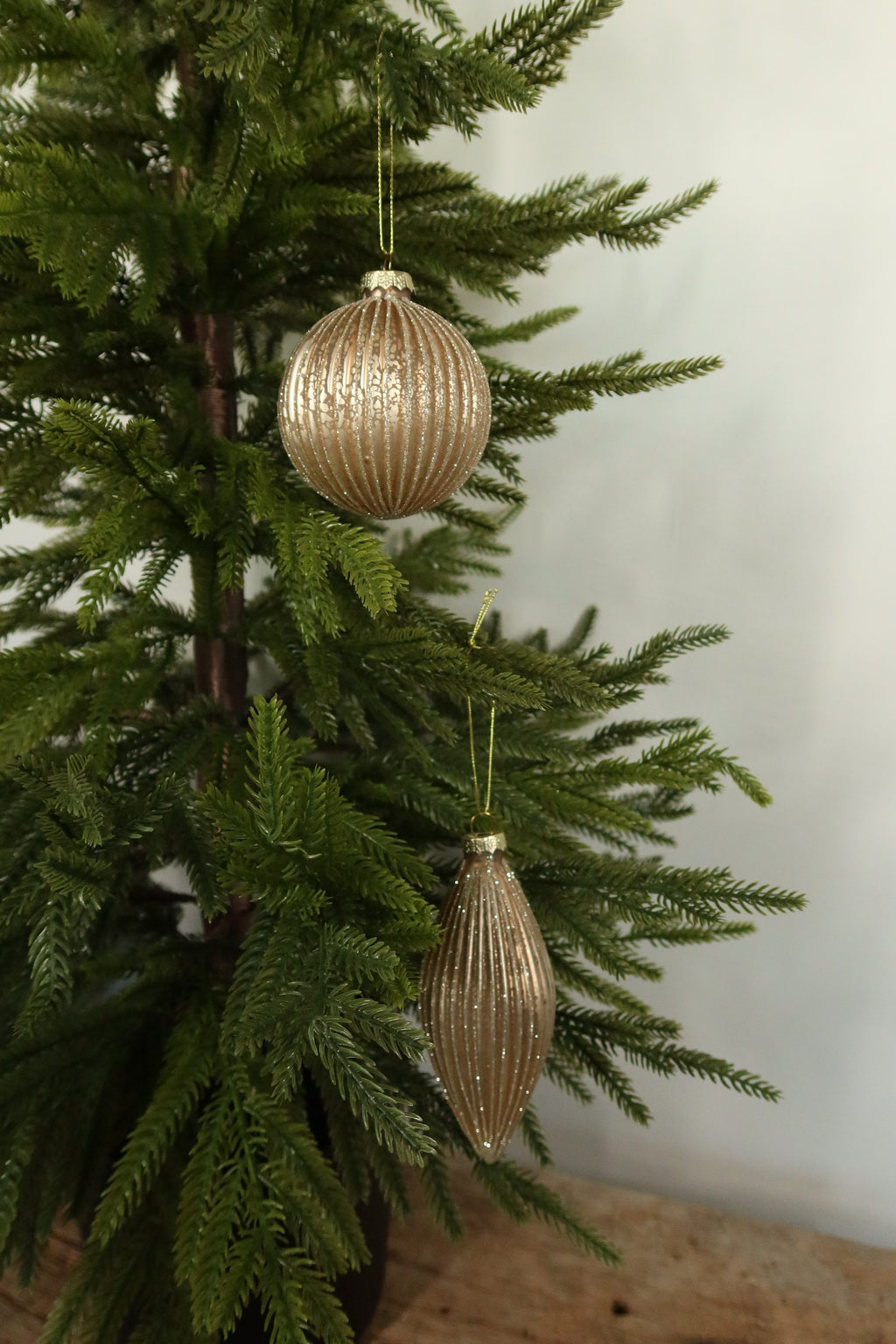 Matte gold fluted glass ball and finial Christmas ornaments with glitter-lined ribs hanging together on an evergreen tree