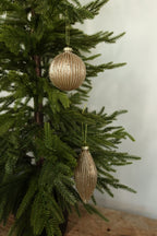 Matte gold fluted glass ball and finial Christmas ornaments with glitter-lined ribs hanging together on an evergreen tree