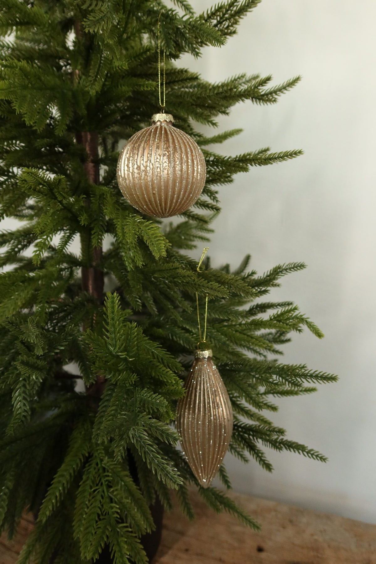 Matte gold fluted glass ball and finial Christmas ornaments with glitter-lined ribs hanging together on an evergreen tree