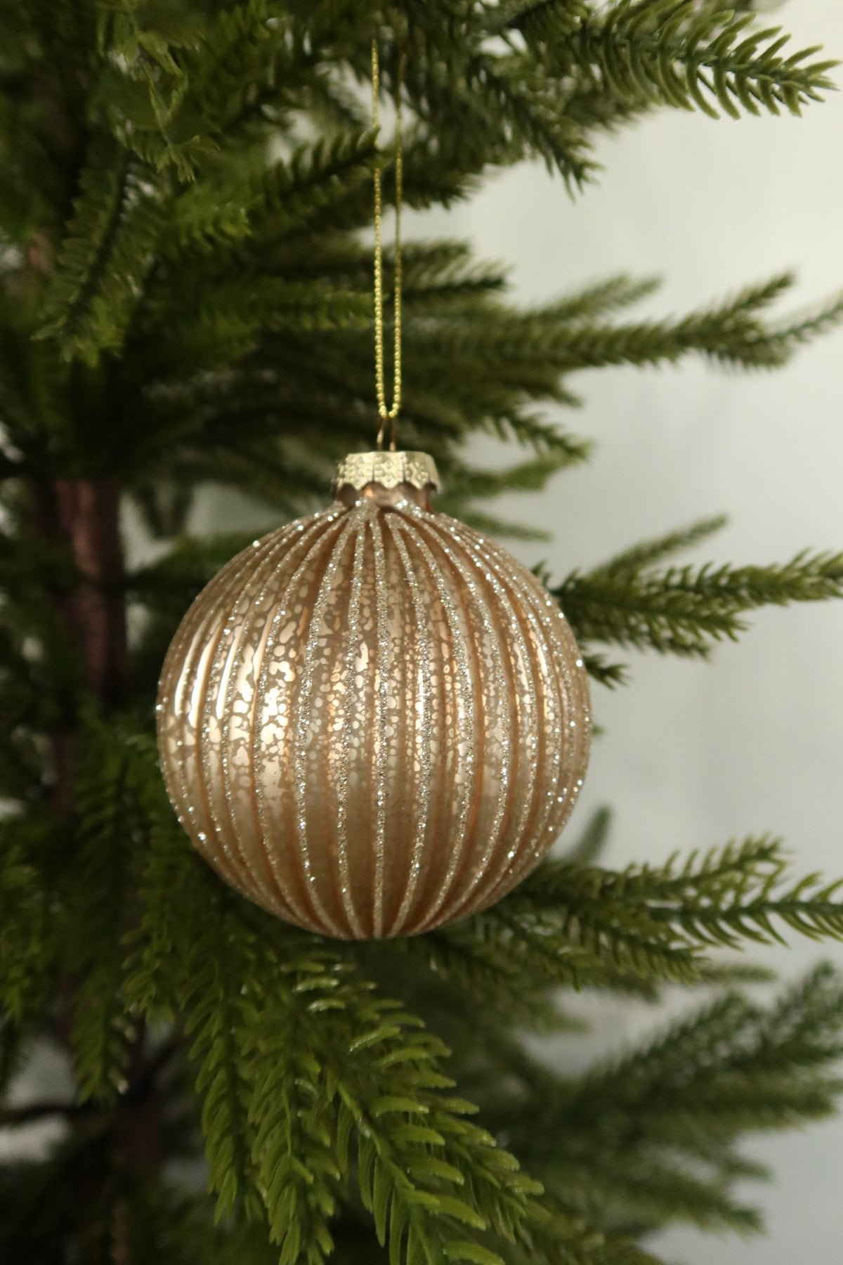 Matte gold fluted glass ball Christmas ornament with glitter-lined ribs hanging on an evergreen tree