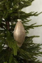 Matte gold fluted glass finial ornament with glitter-lined ribs on a gold cord among green pine branches