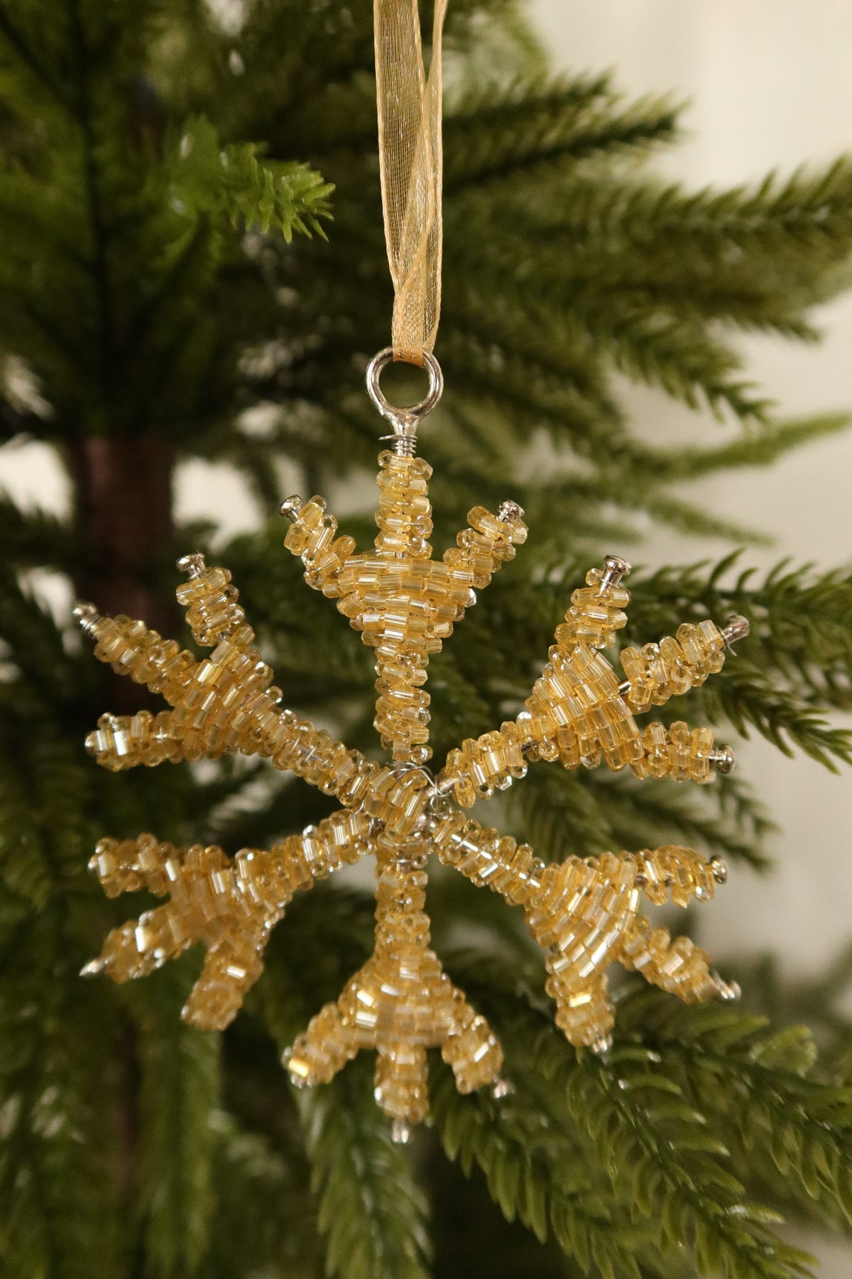 Closer view of the 3.5 inch pale gold beaded snowflake ornament against green pine branches